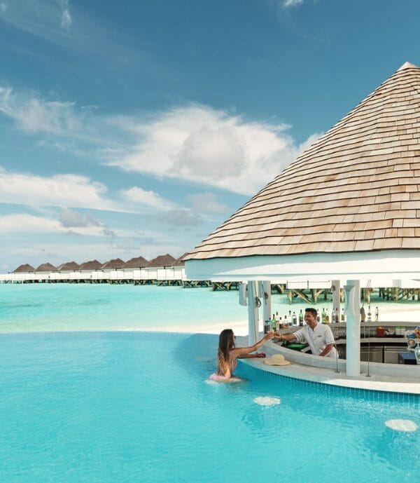 Guest relaxing in a pool getting a drink from a swim up bar at a tropical resort with overwater villas.