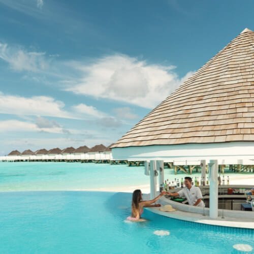 Bartender handing a drink to a woman in the pool from the bar at Solis Pool, Nova Maldives