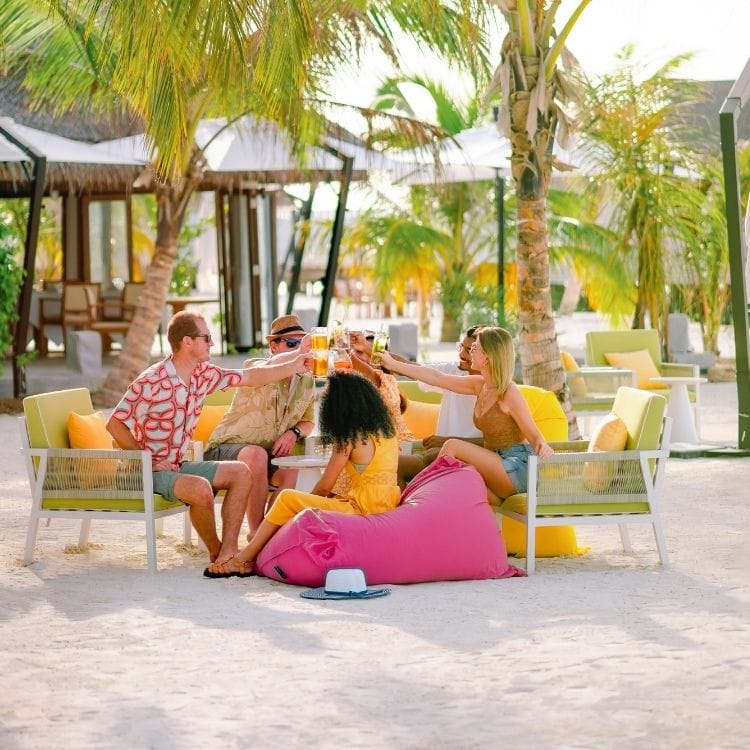 a young group of people sitting on chairs under palm trees with drinks at Wink