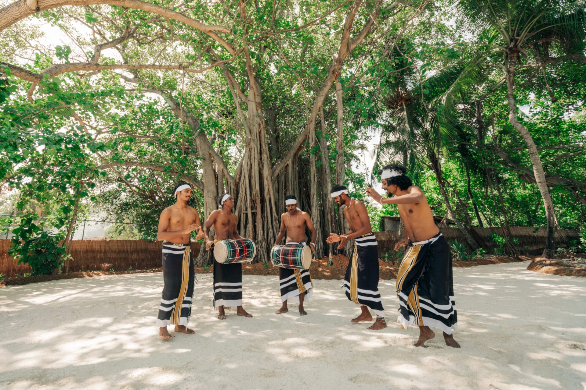 Five men wearing traditional Maldivian clothing, dancing and playing 'bodu beru', a Maldivian drum