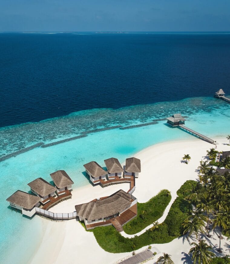 Aerial view of a tropical island with overwater villas and surrounding turquoise waters.
