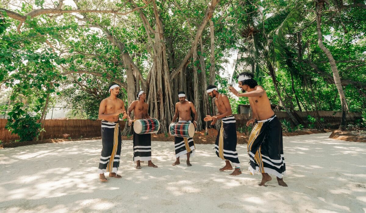 Five men wearing traditional Maldivian clothing, dancing and playing 'bodu beru', a Maldivian drum