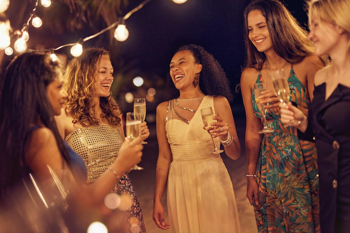 Group of women dressed in evening gowns, celebrating with drinks.