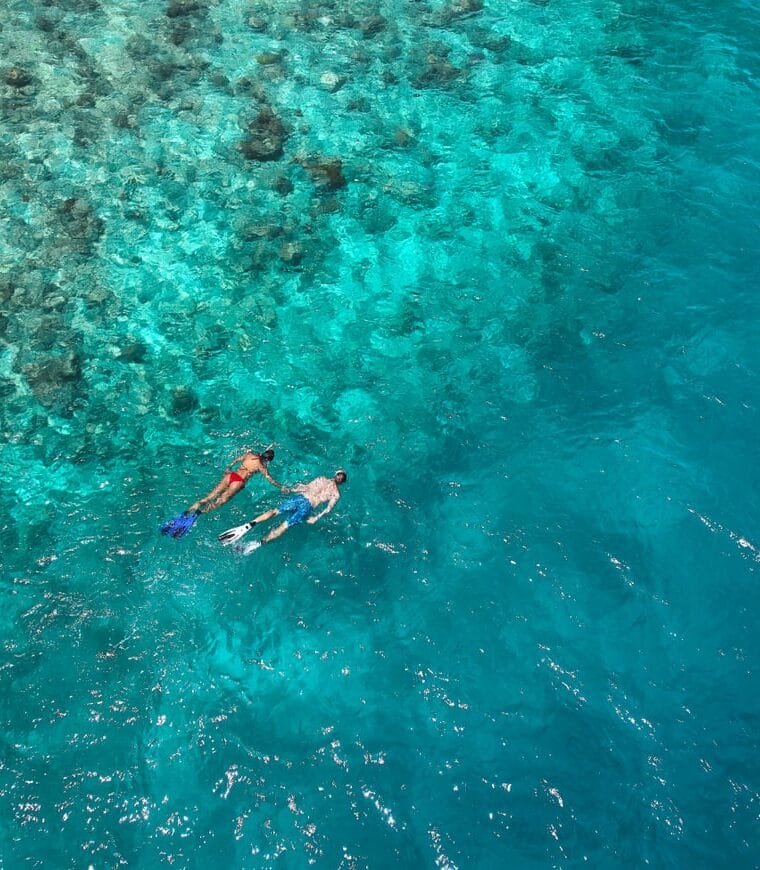 Couple holding hands and snorkeling along the reef in the crystal-clear waters of the Maldives