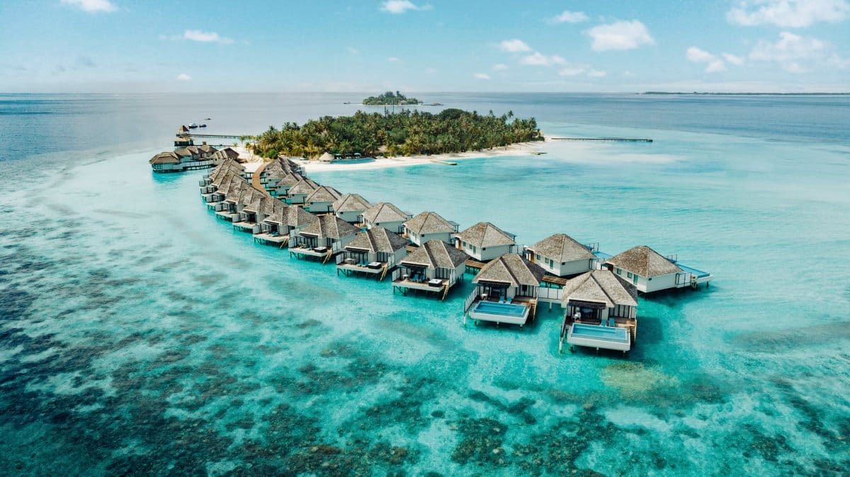 Stunning aerial view of overwater bungalows stretching into the turquoise ocean at a luxury resort.