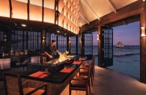 A chef preparing a vibrant teppanyaki dish in an open dining space overlooking the ocean at sunset.